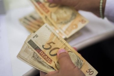 Değişim bürosu / bankada çalışan iş adamının insan eli. O para sayıyor ve bir müşteriye nakit para veriyor. Brezilyalı 50 reais fatura.
