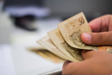 Değişim bürosu / bankada çalışan iş adamının insan eli. O para sayıyor ve bir müşteriye nakit para veriyor. Brezilyalı 50 reais fatura.