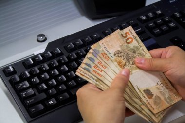 Değişim bürosu / bankada çalışan iş adamının insan eli. O para sayıyor ve bir müşteriye nakit para veriyor. Brezilyalı 50 reais fatura.