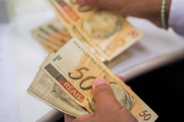 Değişim bürosu / bankada çalışan iş adamının insan eli. O para sayıyor ve bir müşteriye nakit para veriyor. Brezilyalı 50 reais fatura.