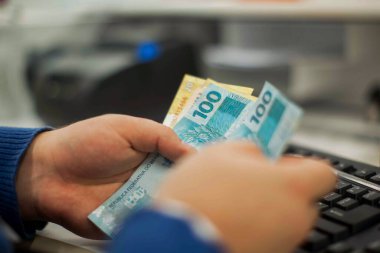 Değişim bürosu / bankada çalışan iş adamının insan eli. O para sayıyor ve bir müşteriye nakit para veriyor. Brezilya Reais 100 reais.