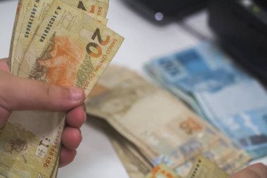 Değişim bürosu / bankada çalışan iş adamının insan eli. O para sayıyor ve bir müşteriye nakit para veriyor. Brezilya Reais - 20 reais fatura.