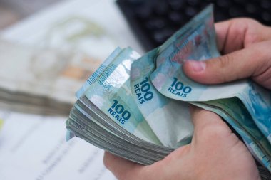 Değişim bürosu / bankada çalışan iş adamının insan eli. O para sayıyor ve bir müşteriye nakit para veriyor. Brezilya Reais 100 reais.