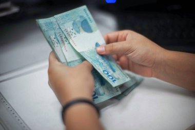 Değişim bürosu / bankada çalışan iş adamının insan eli. O para sayıyor ve bir müşteriye nakit para veriyor. Brezilya Reais 100 reais.