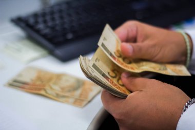 Değişim bürosu / bankada çalışan iş adamının insan eli. O para sayıyor ve bir müşteriye nakit para veriyor. Brezilyalı 50 reais fatura.
