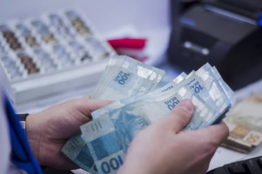 Değişim bürosu / bankada çalışan iş adamının insan eli. O para sayıyor ve bir müşteriye nakit para veriyor. Brezilya Reais 100 reais.