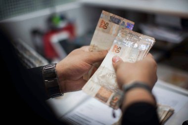 Değişim bürosu / bankada çalışan iş adamının insan eli. O para sayıyor ve bir müşteriye nakit para veriyor. Brezilyalı 50 reais fatura.