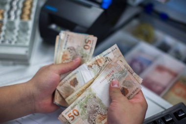 Değişim bürosu / bankada çalışan iş adamının insan eli. O para sayıyor ve bir müşteriye nakit para veriyor. Brezilyalı 50 reais fatura.