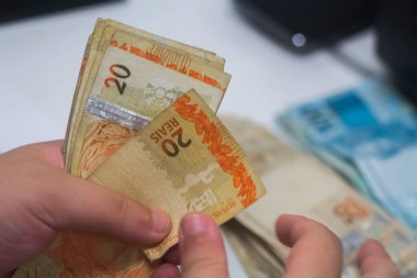 Değişim bürosu / bankada çalışan iş adamının insan eli. O para sayıyor ve bir müşteriye nakit para veriyor. Brezilya Reais - 20 reais fatura.