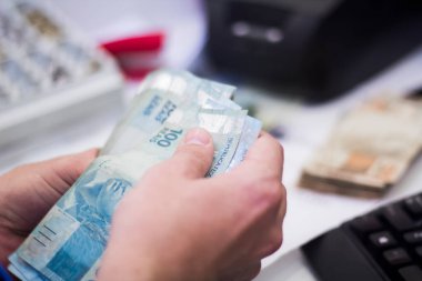 Değişim bürosu / bankada çalışan iş adamının insan eli. O para sayıyor ve bir müşteriye nakit para veriyor. Brezilya Reais 100 reais.