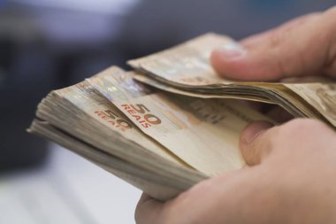Değişim bürosu / bankada çalışan iş adamının insan eli. O para sayıyor ve bir müşteriye nakit para veriyor. Brezilyalı 50 reais fatura.