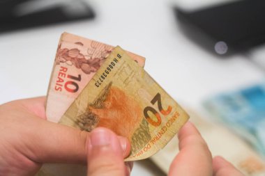 Değişim bürosu / bankada çalışan iş adamının insan eli. O para sayıyor ve bir müşteriye nakit para veriyor. Brezilyalı Reais.