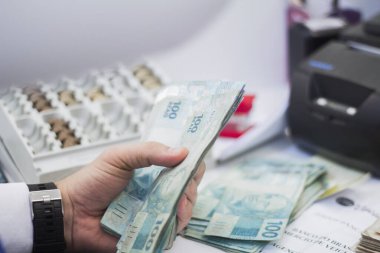 Değişim bürosu / bankada çalışan iş adamının insan eli. O para sayıyor ve bir müşteriye nakit para veriyor. Brezilya Reais 100 reais.
