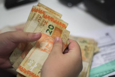 Değişim bürosu / bankada çalışan iş adamının insan eli. O para sayıyor ve bir müşteriye nakit para veriyor. Brezilya Reais - 20 reais fatura.