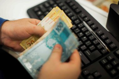Değişim bürosu / bankada çalışan iş adamının insan eli. O para sayıyor ve bir müşteriye nakit para veriyor. Brezilyalı Reais.