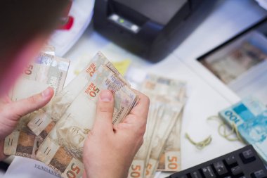 Değişim bürosu / bankada çalışan iş adamının insan eli. O para sayıyor ve bir müşteriye nakit para veriyor. Brezilyalı 50 reais fatura.