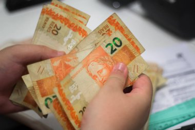 Değişim bürosu / bankada çalışan iş adamının insan eli. O para sayıyor ve bir müşteriye nakit para veriyor. Brezilya Reais - 20 reais fatura.