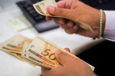 Değişim bürosu / bankada çalışan iş adamının insan eli. O para sayıyor ve bir müşteriye nakit para veriyor. Brezilyalı 50 reais fatura.