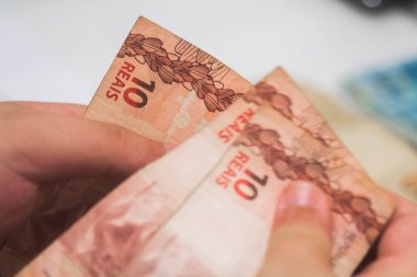 Değişim bürosu / bankada çalışan iş adamının insan eli. O para sayıyor ve bir müşteriye nakit para veriyor. Brezilya Reais - 10 reais fatura.