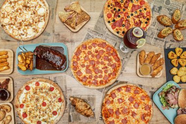 Fast food yemekleri ve dört peynirli aile pizzaları, jambon ve ananas, taze pişmiş sosisler, barbekü kaburgaları, sarımsaklı tavuk kanatları ve gazete sayfalarında peynir ve sarımsaklı parmaklar.