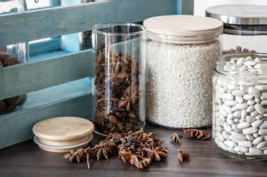 Baharat kavanozları, baharatlar, çiğ pirinç, yıldız anasonu ve baklagiller ahşap bir yüzey ve arkasında mavi bir kulübe.