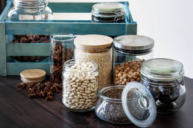 Bir sürü baharatlı cam kavanoz, mısır gevreği, chia, yıldız anason ve mavi tahta kutu.