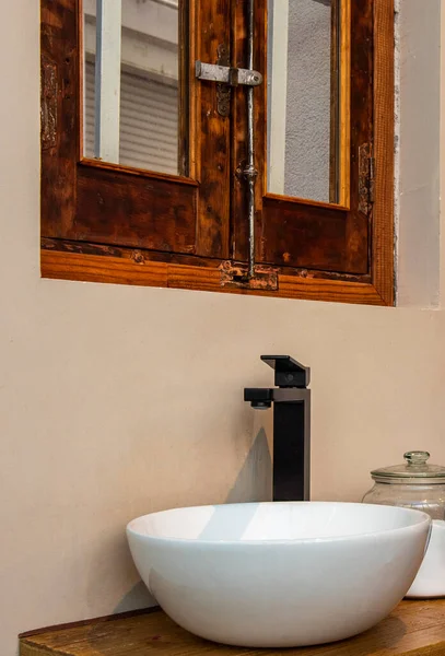 White porcelain sink with black faucet under wooden window