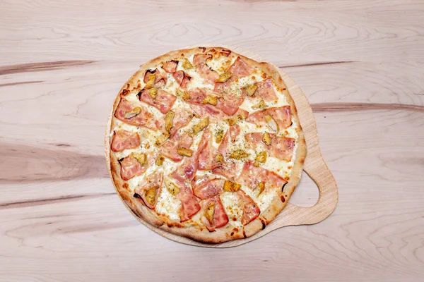 Family carbonara recipe pizza with a lot of mozzarella cheese and york ham on an unvarnished wooden table