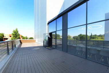 Metal parmaklıkları ve büyük cam ve metal yüzeyleri olan, ahşap zemini olan boş bir teras.