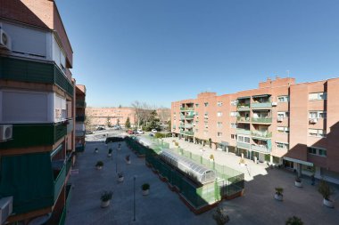 Tuğla bina cepheleri ve dairesel çimento ekicileri olan bir halk meydanı manzarası.