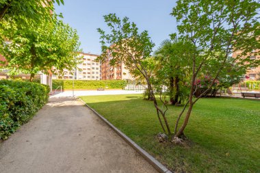 Güneşli bir günde ağaçların, bahçelerin, çimenlerin, çiçeklerin ve yüzme havuzunun arasına cephe manzaralı şehir parkı.