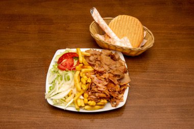 Tipik kebap tabağı, karışık kuzu eti, tavuk, beyaz soğan ve marulla birlikte beyaz tabakta patates kızartması ve sepette çatal bıçakla birlikte ekmek.
