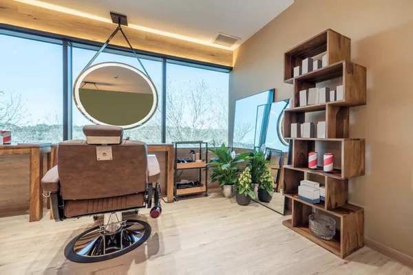 Corner of a beauty salon with a brown hairdressing chair and a circular mirror with leds