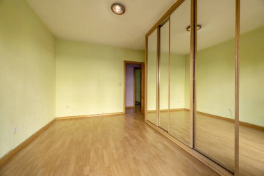 Kaplamalı döşemeleri olan boş bir oda ve sürgülü ayna kapıları ve meşe ağacından kenarları olan gardıropla kaplı bir duvar.