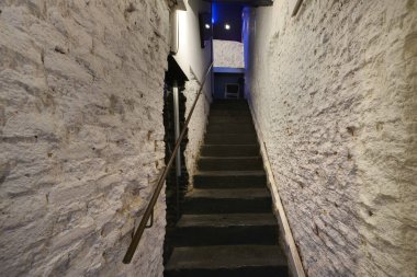 Beyaz tuğlalı duvarları ve metal parmaklıklı siyah taş basamakları olan bir gece kulübünün merdiveni.