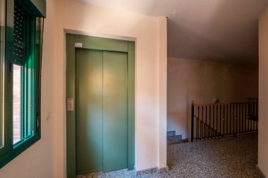 Granit zemini, ahşap korkuluğu ve yeşil boyalı asansörü olan bir apartman dairesi.