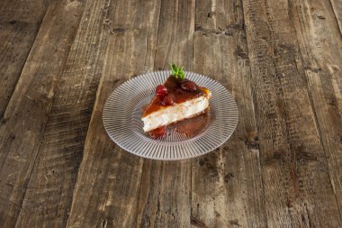 Çilek şurubuyla nefis bir porsiyon cheesecake ve verniklenmemiş ahşap masa üzerinde şekerli çilek.