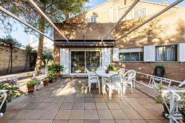 Aynı masa ve sandalyelerle dolu yemek odası olan bir villanın arka bahçesi.