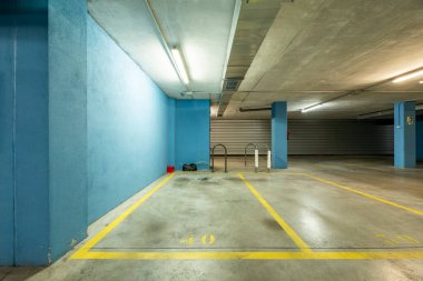 Boş garaj alanı, gri beton zemin, sarı çizgiler ve mavi boyalı duvarlar.