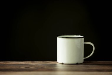 Tahta bir masanın üzerinde beyaz bir mineli metal kahve fincanı.