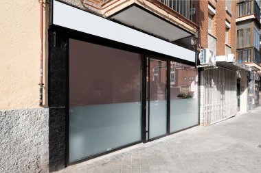 Camları ve siyah metali olan kaldırımlı bir caddeden görülen ticari bir binanın ön cephesi