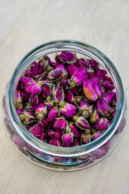 Hafif ahşap bir yüzeyde kurumuş çay gülleriyle dolu cam bir kavanoz.