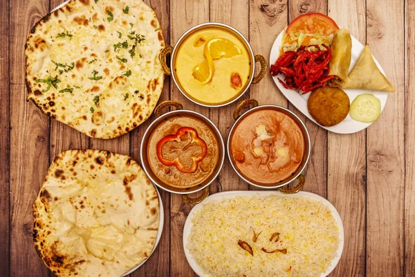 A still life of Indian food dishes with chicken and lamb curry, basmati rice, cheese and garlic naan and appetizer plate with fried onion and samosa
