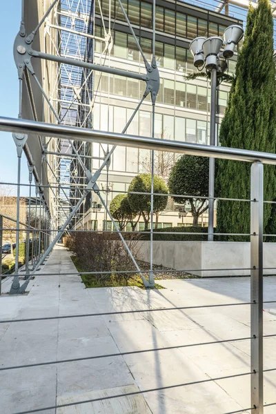 Metal and glass facade with metal frames, railing with steel cables and covered gardens at the entrance of an office building