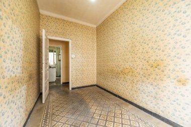 Duvarları eski ve kirli duvar kağıtlarıyla kaplı bir yatak odası, aşınmış hidrolik taş kaplama döşemeler ve beyaz ahşap kapılar.