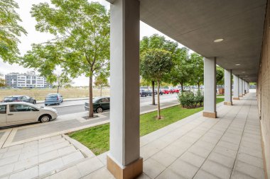 Porch of a building with an illuminated, tree-lined promenade and gardens with hedges and lawns