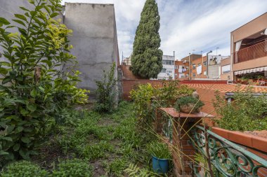 Interior patio with exposed mud bricks, pots made of the same material, wrought iron railing, trees and many plants in individual pots