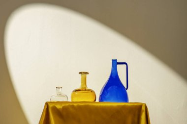 Decorative glass jars of different colors on a golden fabric structure under the light of a spotlight