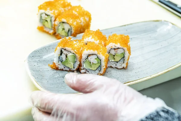 An Asian sushi chef assembling a tray with a uramaki california roll with masago roe