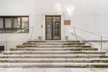 Stone stairs leading up to a building with a white marble facade and a brown anodized aluminum door